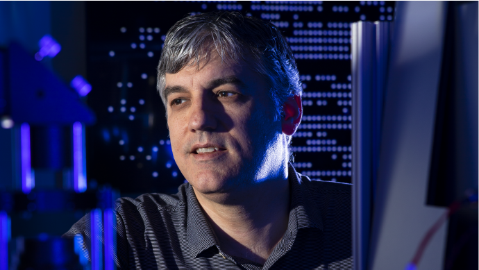 Photograph of Christopher Monroe in a dim laboratory with blue light shining around him.