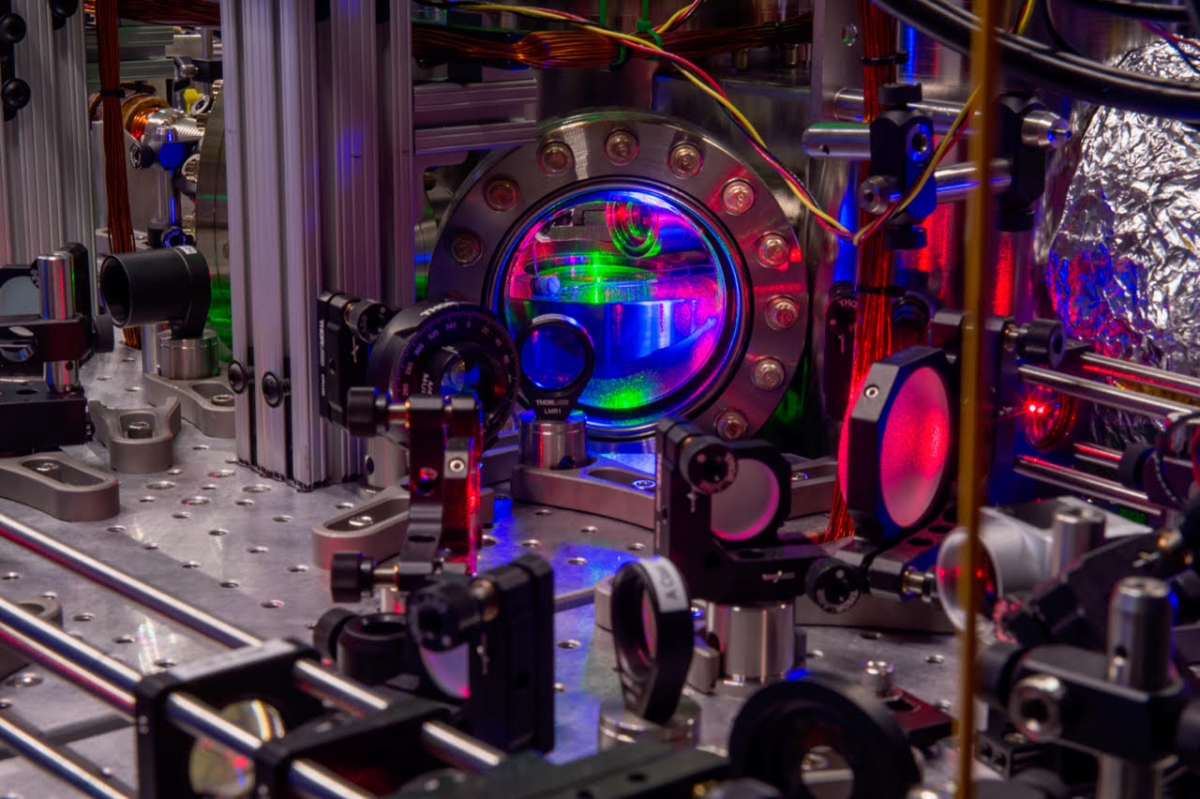 Red, green and purple lights shine through a window of a metallic chamber and off scientific optical equipment.