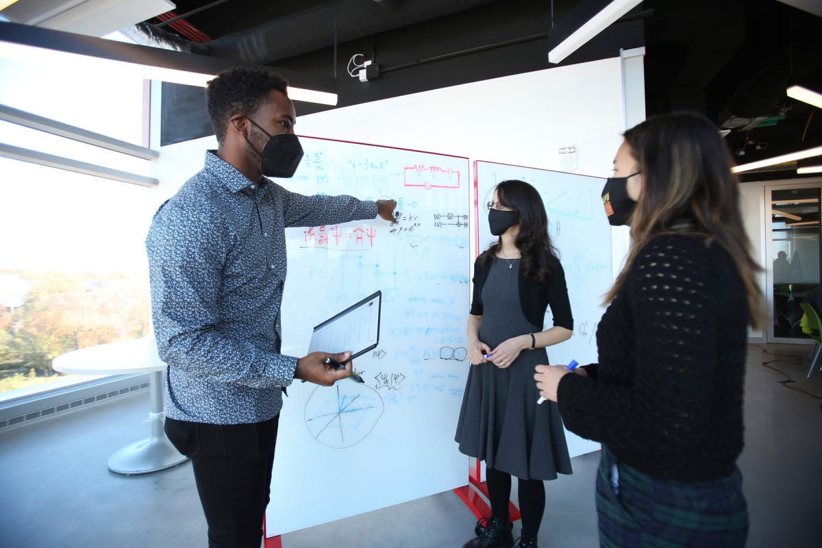 A man and two women stand in front of a whiteboard