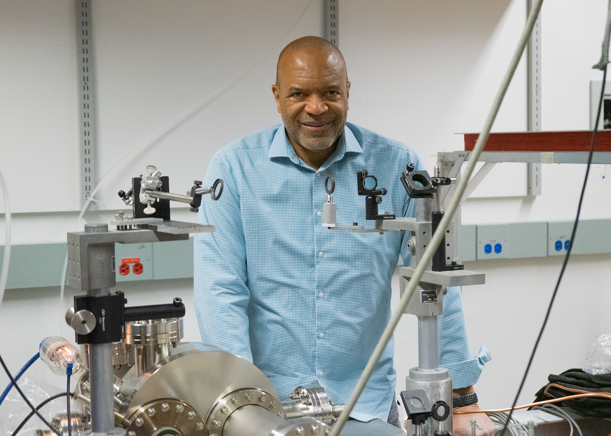 Wendell Hill III wearing a blue shirt stands behind wires and stainless steal science equipment.