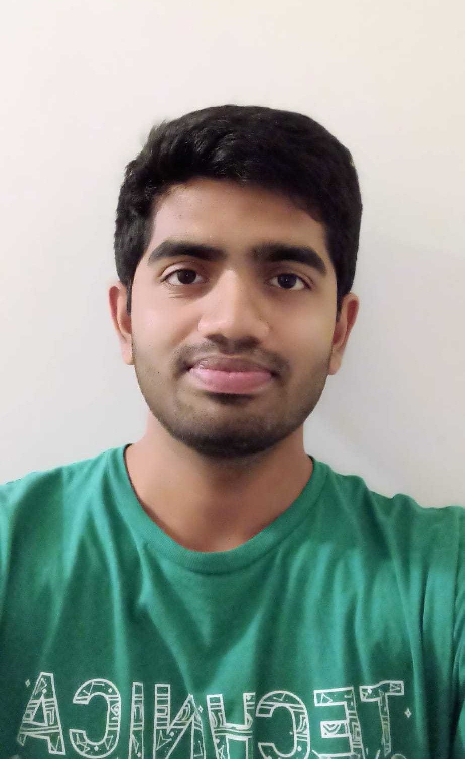 A smiling young man appears, with brown skin and black hair, wearing a green t-shirt.