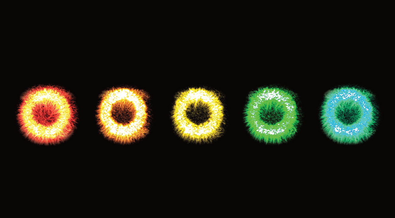 Five glowing rings with flame like filaments in a row against a black background. From left to right they are reddish-orange, orange, yellow, green and a greenish-blue.