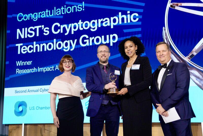 Carl Miller and Angela Robinson (second and third from left, respectively) accepting the research impact award on behalf of the NIST Cryptographic Technology Group for their work on post-quantum cryptography.